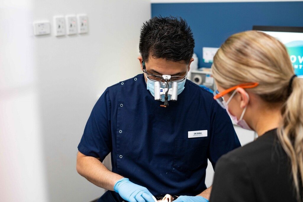 A male and female dentist in masks collaborate on endodontics procedures for a tooth in a dental clinic.