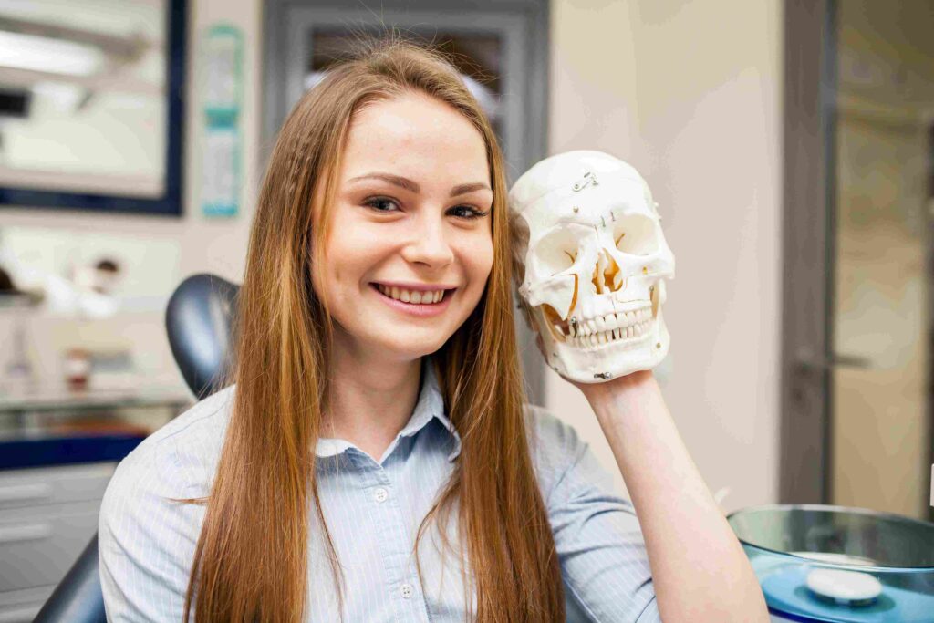 A woman smiles confidently while holding a skull, symbolizing the impact of Temporomandibular Joint Surgery.