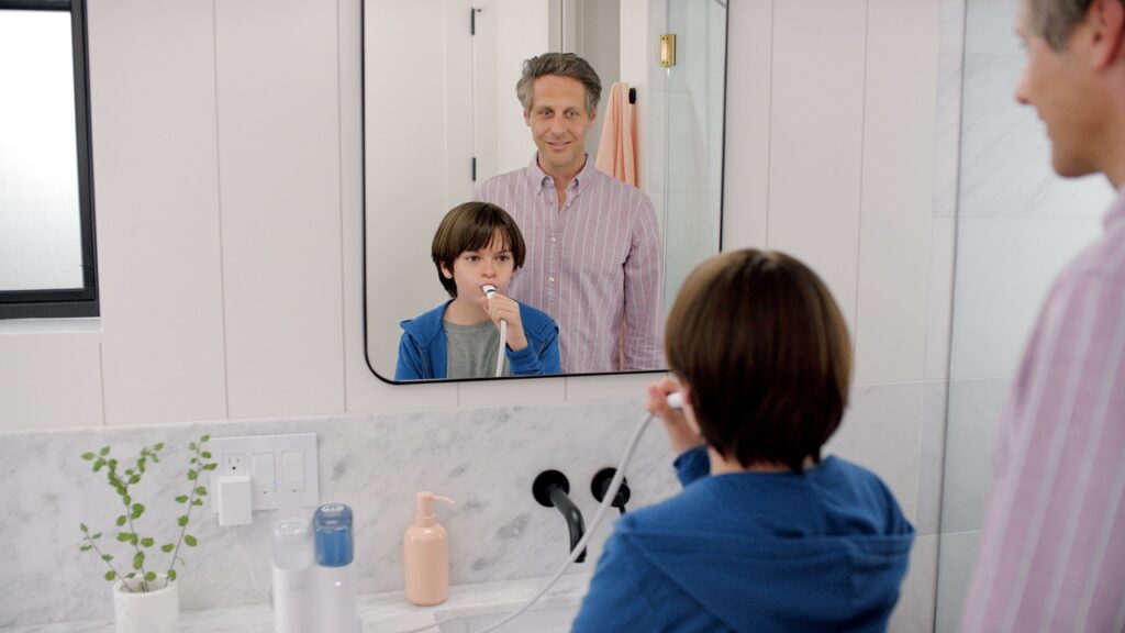 A man practices good oral hygiene by brushing his teeth in front of a mirror, emphasizing the importance of pediatric dentistry.