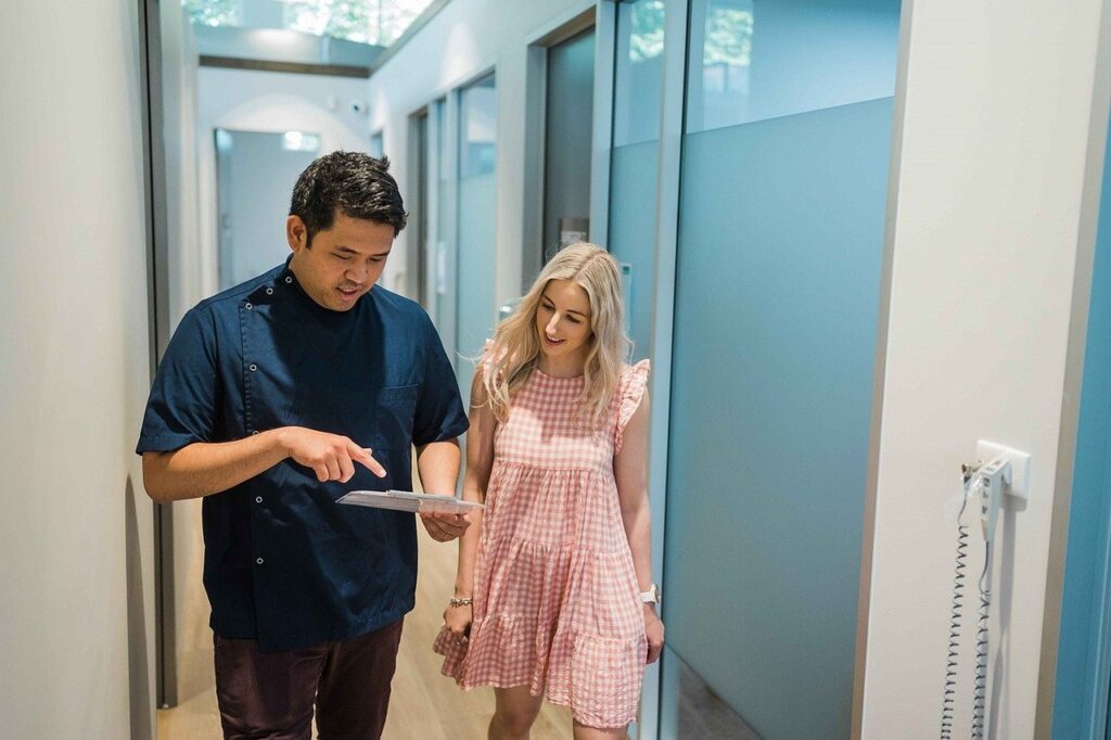 A man and woman walk down a hallway, holding a tablet, discussing root canal treatment options.